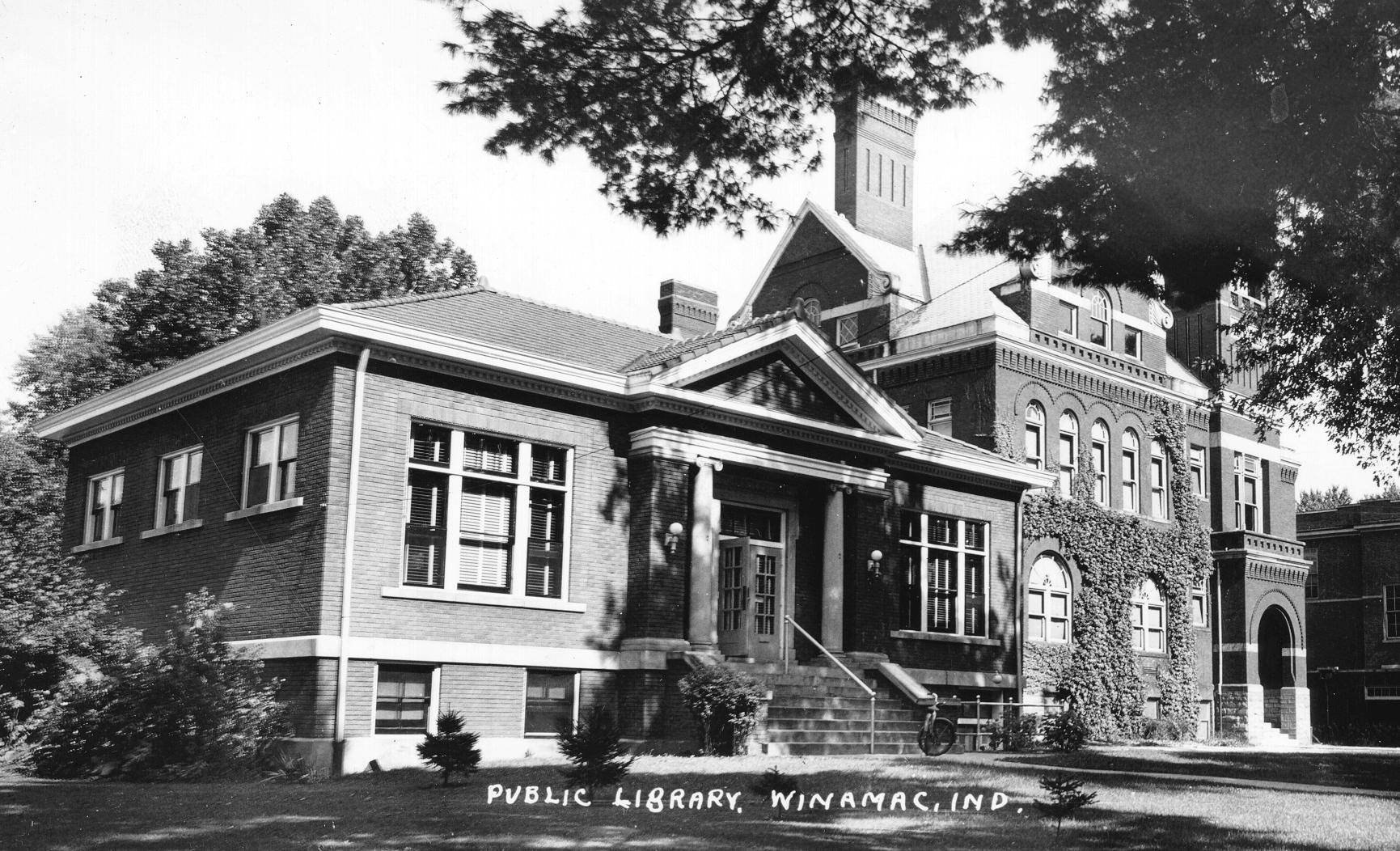 Black & white photo of the Carnegie Library in Winamac with Winamac Elementary School in the background.