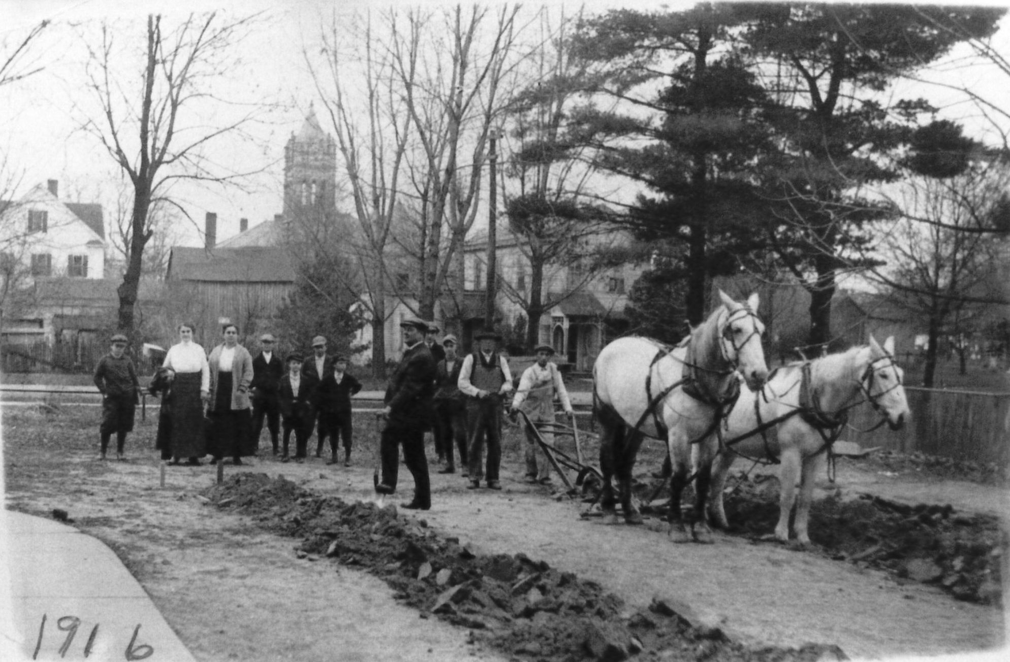 Black & white photo from 1916 showing several people, two horses, and a plow at the groundbreaking of the Winamac Carnegie Library.