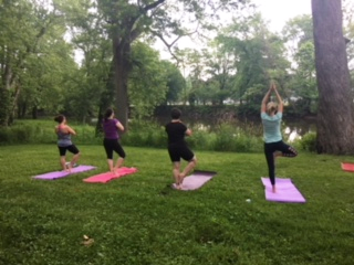Four women doing yoga outdoors next to the Tippecanoe River.