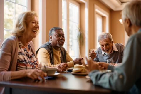 older adults sitting around a table eating and laughing, enjoying each others' company