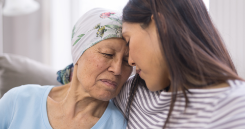 a young woman holding sitting next to an older woman wearing a scarf over her head, hugging her and touching foreheads together