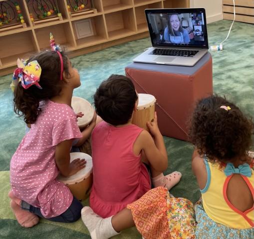 children watching a screen and taking part in a live Zoom class through Playgarden Prep