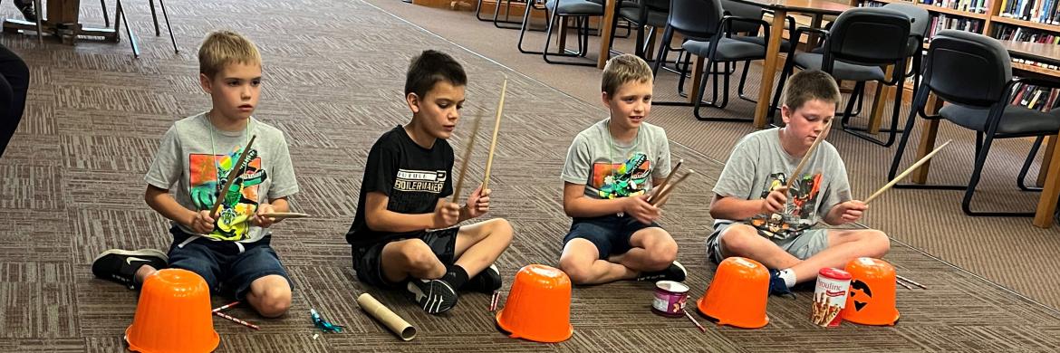 four kids drumming during music event in the library