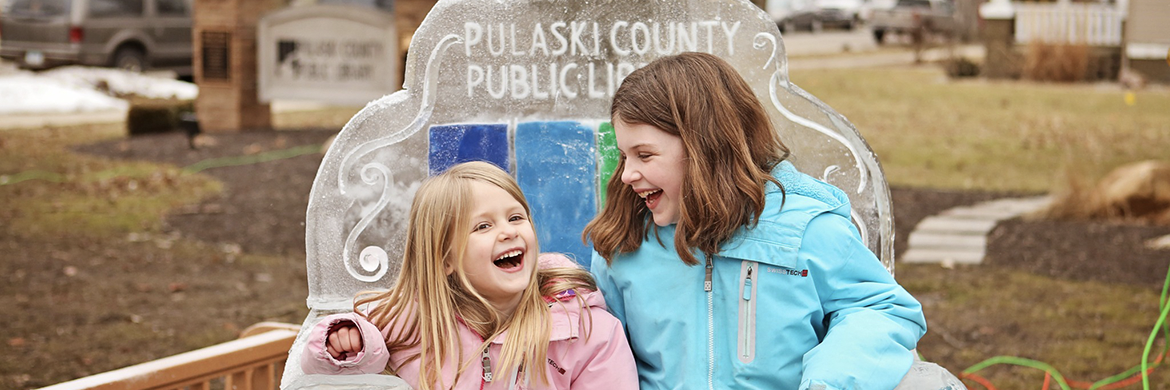 Two girls laughing and sitting on an ice-sculpted chair