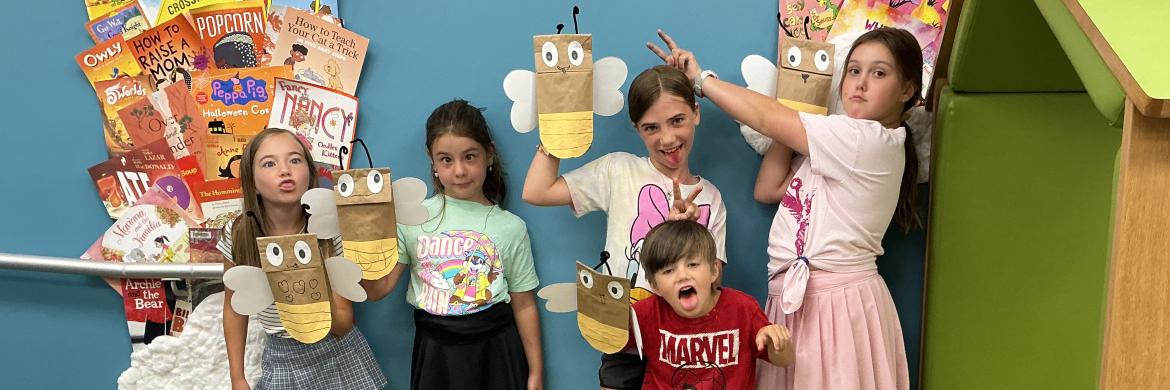 a group of children making silly faces and holding up firefly puppets they made at the library